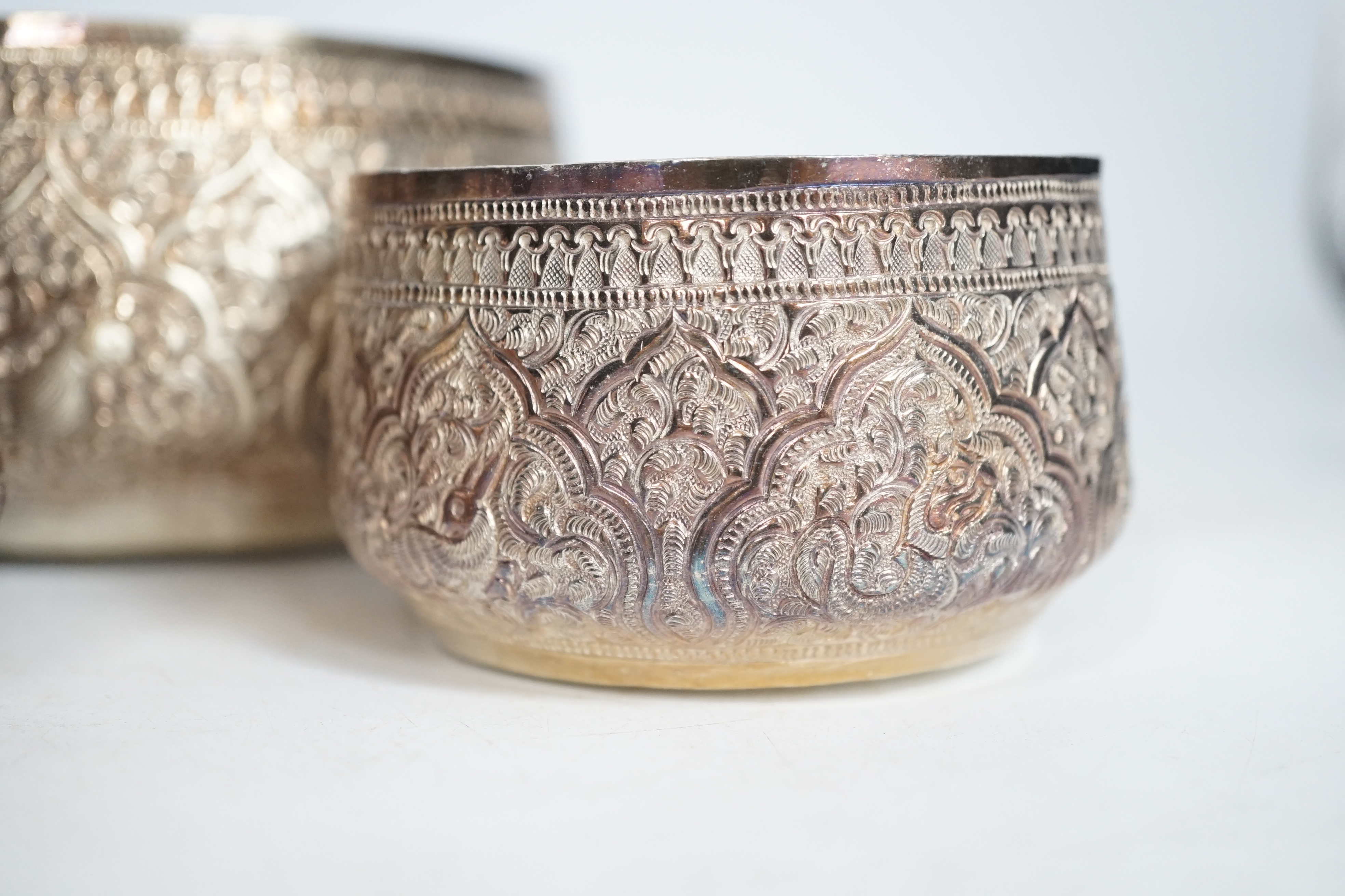 A pair of Thai circular white metal bowls, and a pair of small bowls, all decorated with animals and foliate scrolls, inscribed on bases, diameter 12cm and 8.5cm